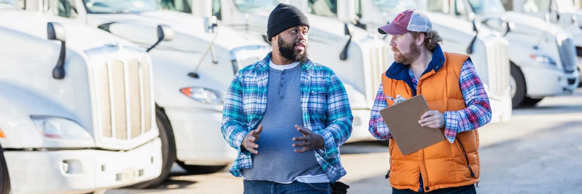 two men walking in front of a fleet of commercial trucks